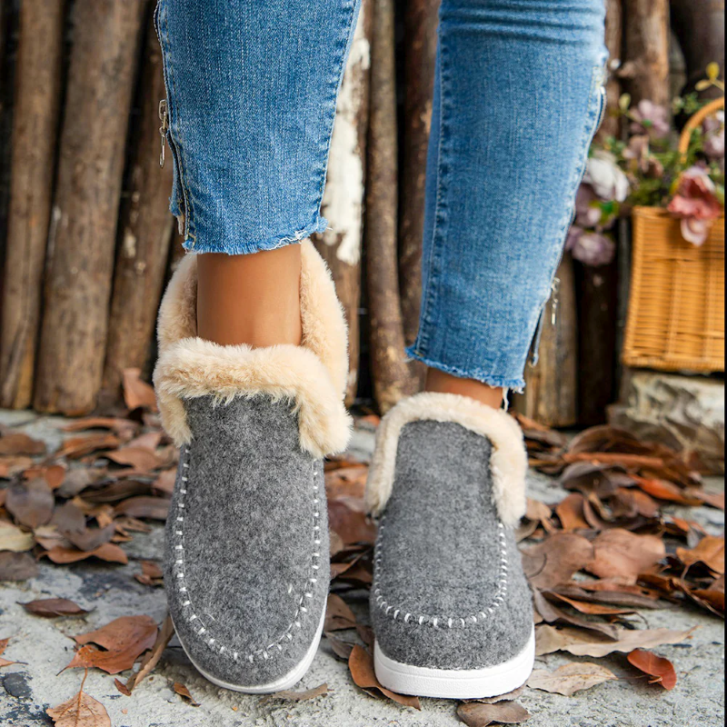 Gray slippers with white fur trim worn with blue jeans on a rustic background.