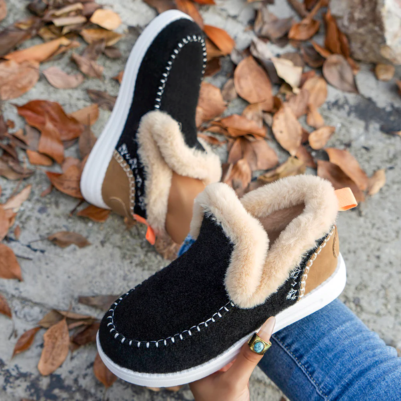 Black and brown winter shoes with fur lining held over a ground covered with autumn leaves.