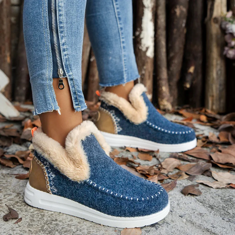 Blue slip-on boots with fur trim worn by a person on a leaf-covered ground.