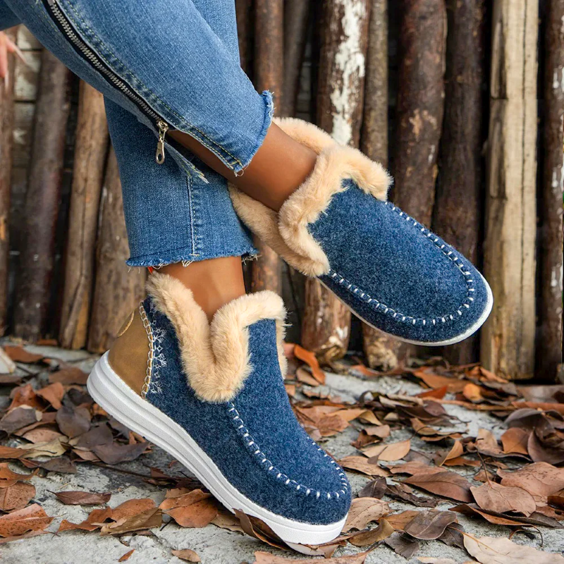 Blue slip-on boots with beige fur trim worn by a person against a rustic wooden background.