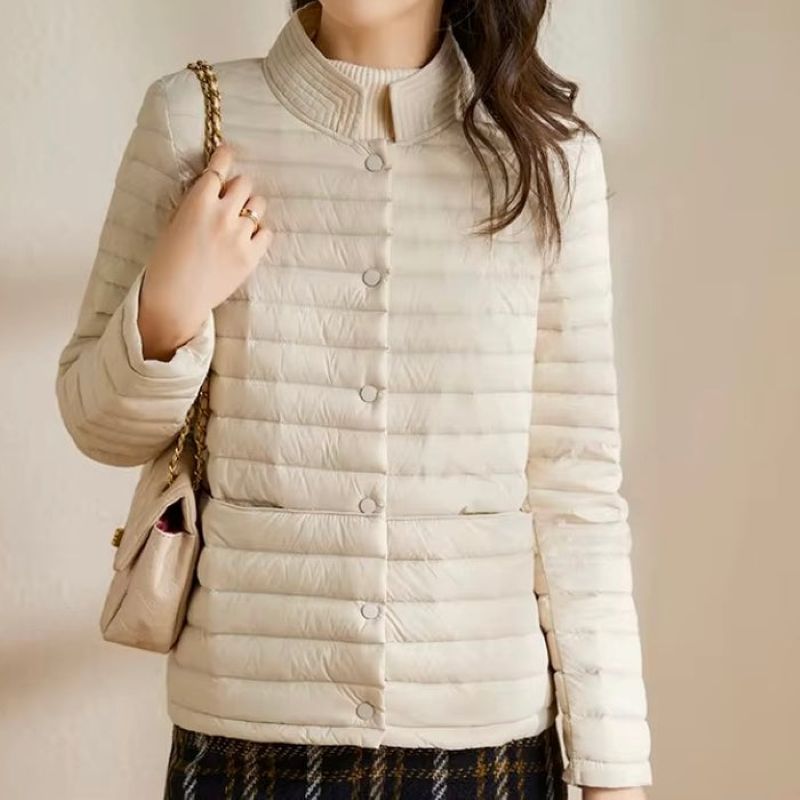 Woman wearing a beige puffer jacket holding a matching handbag against a neutral background