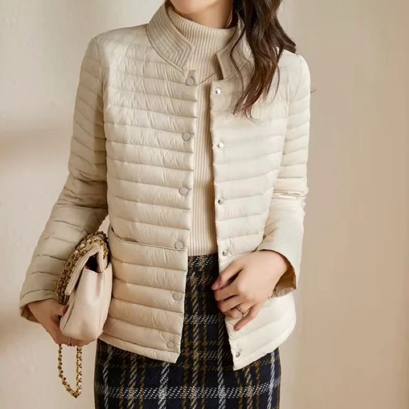 Person wearing a beige puffer jacket holding a handbag against a neutral background