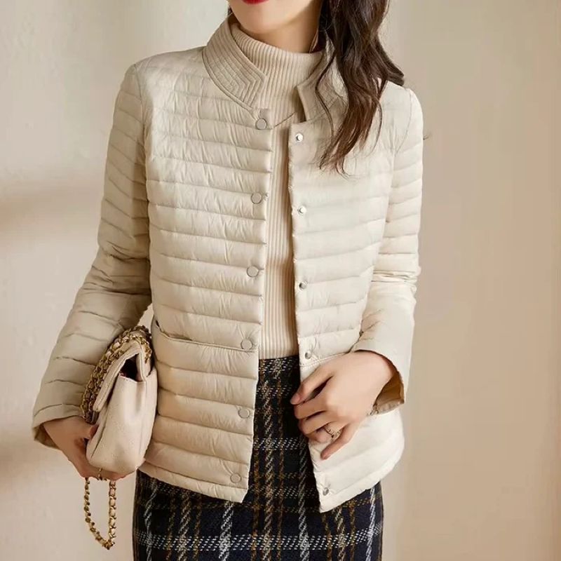 Woman wearing a beige puffer jacket with a plain background