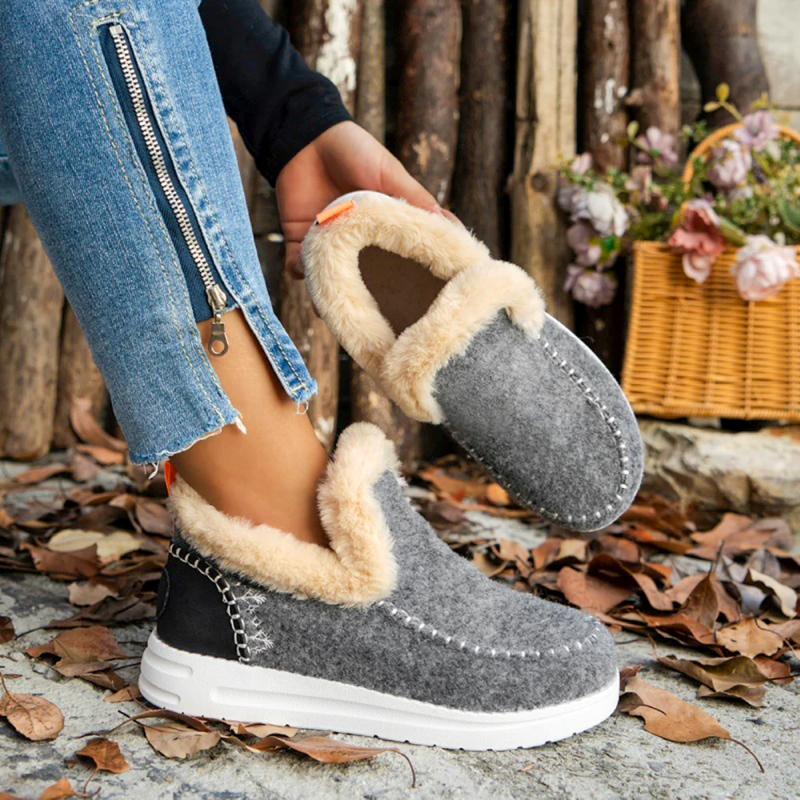 Gray slippers with beige fur lining worn by a person, with a rustic background.