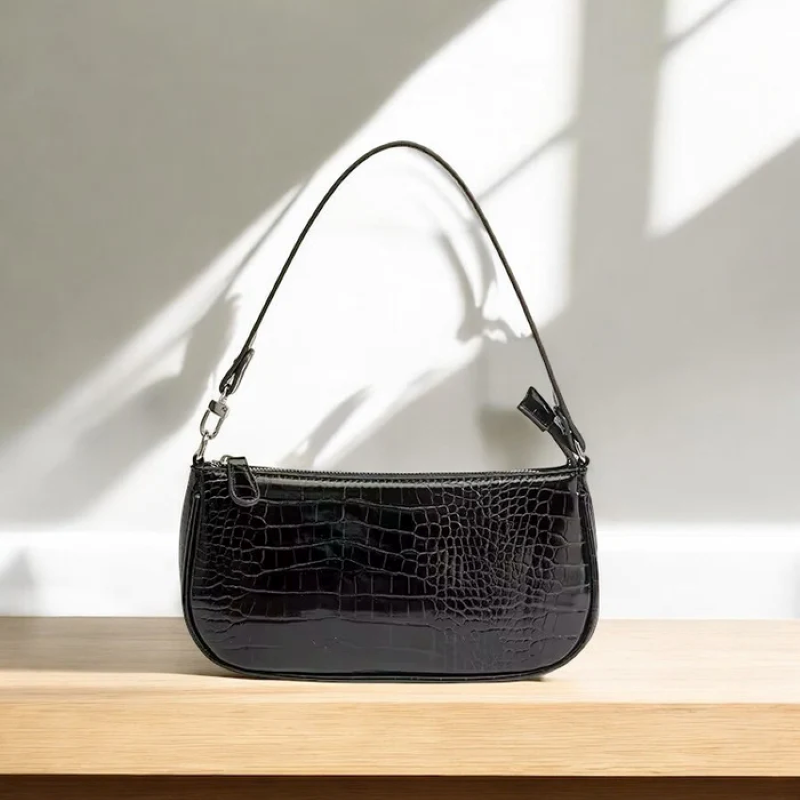 Black crocodile-patterned handbag on a wooden surface with a light background
