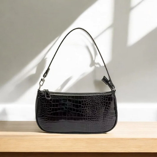 Black crocodile-patterned handbag on a wooden surface with a light background
