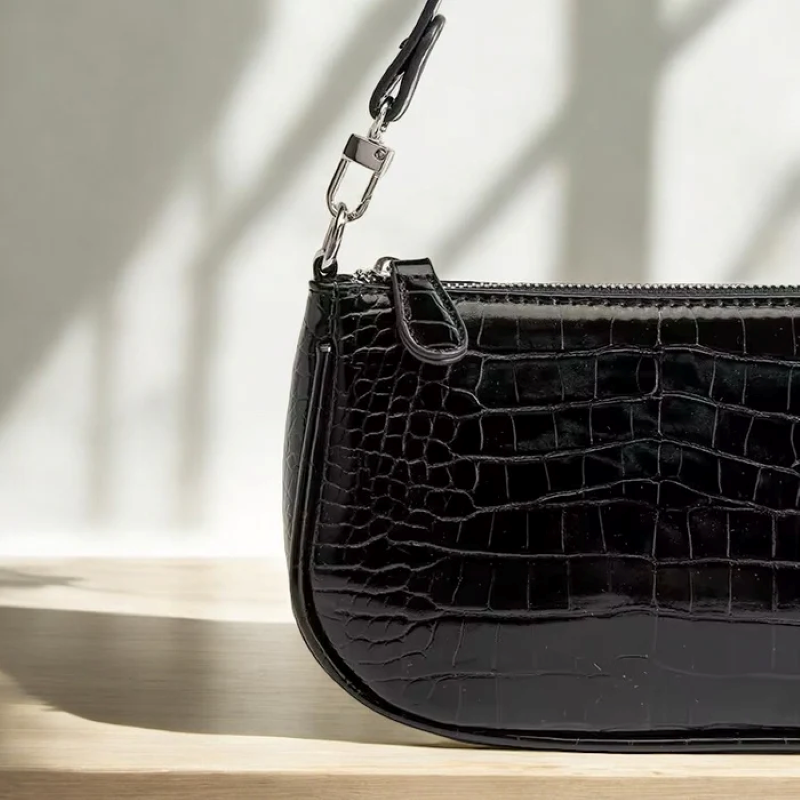 Black crocodile-patterned handbag on a wooden surface with a neutral background