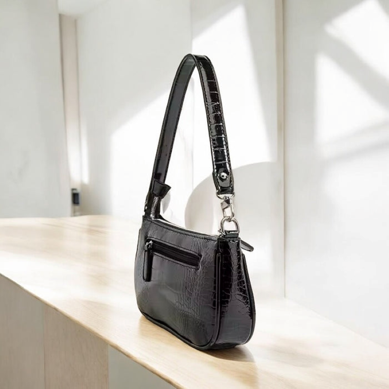Black handbag with a textured pattern on a light wooden surface.