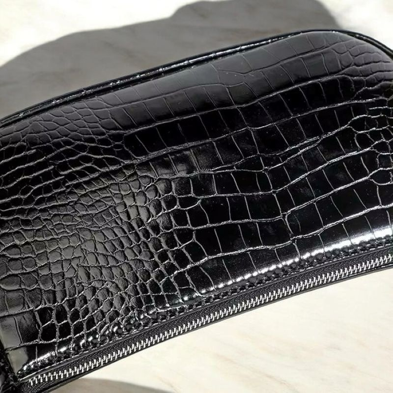 Black crocodile-patterned clutch bag with a zipper on a light background