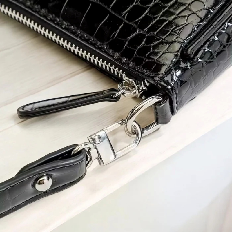 Black crocodile-patterned handbag with a strap on a light wooden surface