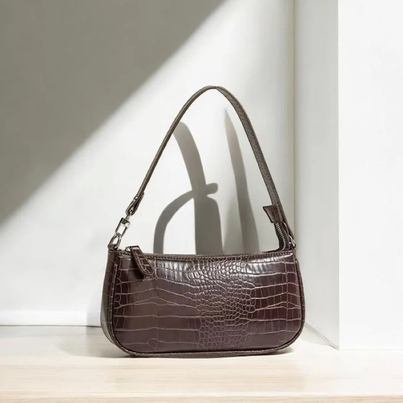 Brown crocodile-patterned handbag on a light wooden surface with a white wall background