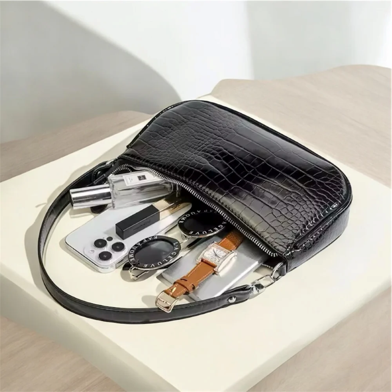 Black crocodile-patterned pouch with various items on a light surface