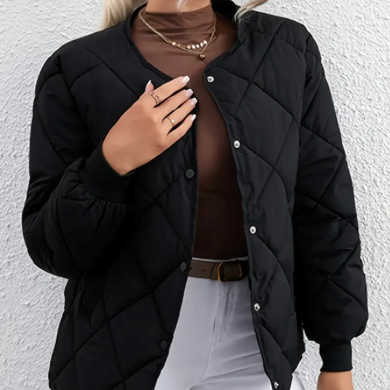 Person wearing a black quilted jacket against a white wall